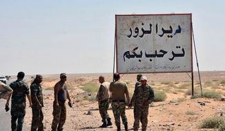 FILE - This file photo released Sept. 3, 2017, by the Syrian official news agency SANA, shows Syrian troops and pro-government gunmen standing next to a sign in Arabic which reads, &quot;Deir el-Zour welcomes you,&quot; in the eastern city of Deir el-Zour, Syria. Syrian state media say the army has liberated the eastern city of Deir el-Zour from the Islamic State group. Friday&#x27;s report says the military is now in full control of the long contested city. (SANA via AP, File)