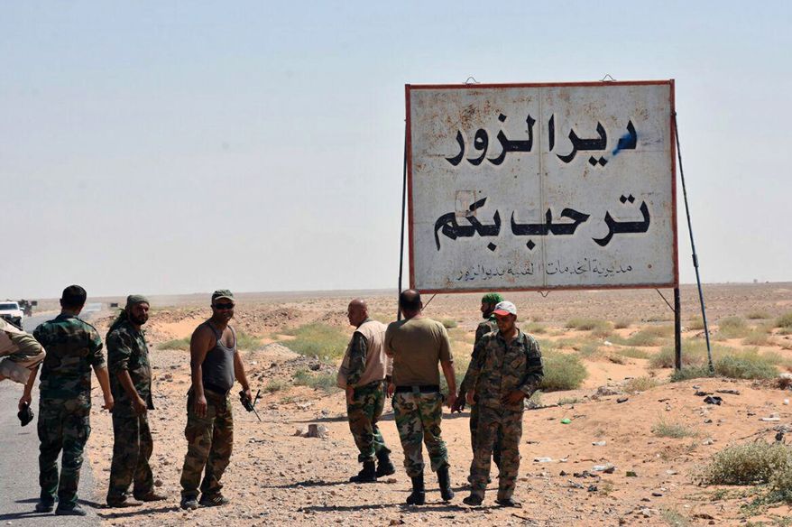 FILE - This file photo released Sept. 3, 2017, by the Syrian official news agency SANA, shows Syrian troops and pro-government gunmen standing next to a sign in Arabic which reads, &quot;Deir el-Zour welcomes you,&quot; in the eastern city of Deir el-Zour, Syria. Syrian state media say the army has liberated the eastern city of Deir el-Zour from the Islamic State group. Friday&#x27;s report says the military is now in full control of the long contested city. (SANA via AP, File)