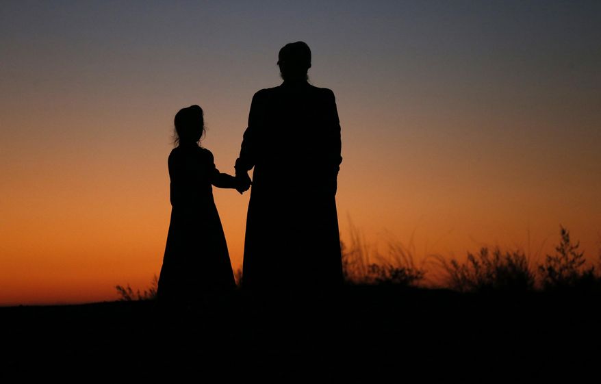 In this Wednesday, Oct. 25, 2017 photo, Lydia Ann, 8, and her mother, Norma Richter, hold hands as they pose for photographs in Colorado City, Ariz. Their community on the Utah-Arizona border has been home for more than a century to members of the Fundamentalist Church of Jesus Christ of Latter-Day Saints, a polygamous sect that is an offshoot of mainstream Mormonism. (AP Photo/Rick Bowmer)