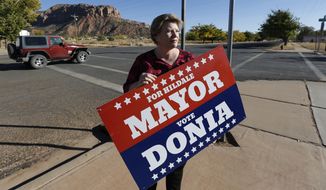 In this Thursday, Oct. 26, 2017 photo, Donia Jessop holds her mayoral campaign sign outside her store in Colorado City, Ariz. Campaign signs are unusual in a town where elections have long been quietly decided behind the scenes, with hand-picked men from the Fundamentalist Church of Jesus Christ of Latter-Day Saints running unopposed. (AP Photo/Rick Bowmer)
