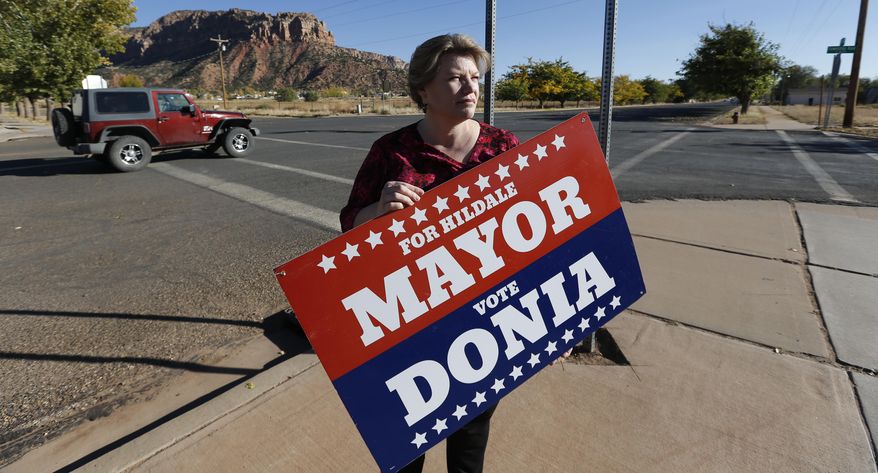In this Thursday, Oct. 26, 2017 photo, Donia Jessop holds her mayoral campaign sign outside her store in Colorado City, Ariz. Campaign signs are unusual in a town where elections have long been quietly decided behind the scenes, with hand-picked men from the Fundamentalist Church of Jesus Christ of Latter-Day Saints running unopposed. (AP Photo/Rick Bowmer)