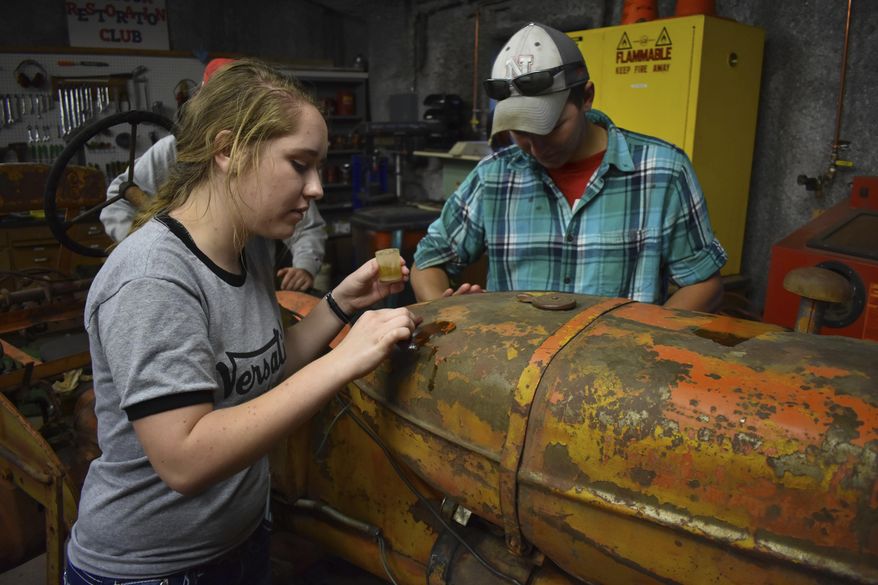 ADVANCE FOR USE SATURDAY, NOV. 4 - In this recent photo, University of Nebraska tractor restoration club members Trisha Hruska, left, and Jaythen Scheideler clean a tractor once owned by the last homesteader with mineral spirits in Beatrice, Neb. The tractor will be on display at Homestead National Monument of America next month. (Scott Koperski/Beatrice Daily Sun via AP)