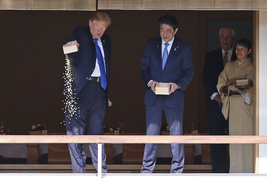 U.S. President Donald Trump pours out the remaining  fish food from a container as he feeds carp at a koi pond with Japan&#x27;s Prime Minister Shinzo Abe, third from right, before their working lunch at Akasaka Palace in Tokyo, Japan Monday, Nov. 6, 2017. (Toru Hanai/Pool Photo via AP)