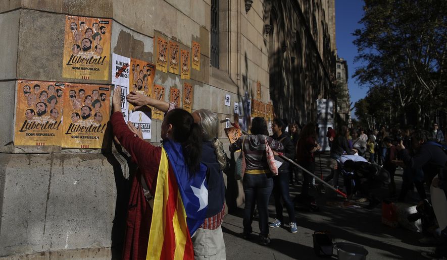 A woman with an 'Estelada', the pro-independence Catalan flag draped over her shoulder, pastes banners on a wall that read in Catalan: "Freedom for the Political Prisoners" during a protest against the decision of a judge to jail ex-members of the Catalan government at the University square in Barcelona, Spain, Sunday, Nov. 5, 2017. A Spanish judge issued an international arrest warrant on Friday for former members of the Catalan Cabinet who were last seen in Brussels, including the ousted separatist leader Carles Puigdemont, who said he was prepared to run for his old job even while battling extradition in Belgium. (AP Photo/Manu Fernandez)