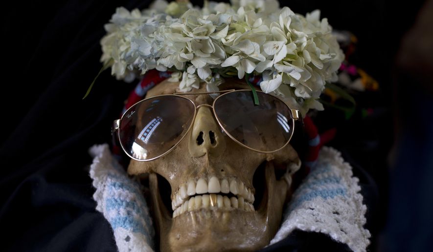A human skull wearing sun glasses is displayed outside the General Cemetary chapel during the Natitas Festival in La Paz, Bolivia, Wednesday, Nov. 8, 2017. Every year, hundreds of Bolivians carry human skulls adorned with flowers to a cemetery in La Paz, asking for money, health, and other favors as part of a festival. (AP Photo/Juan Karita)