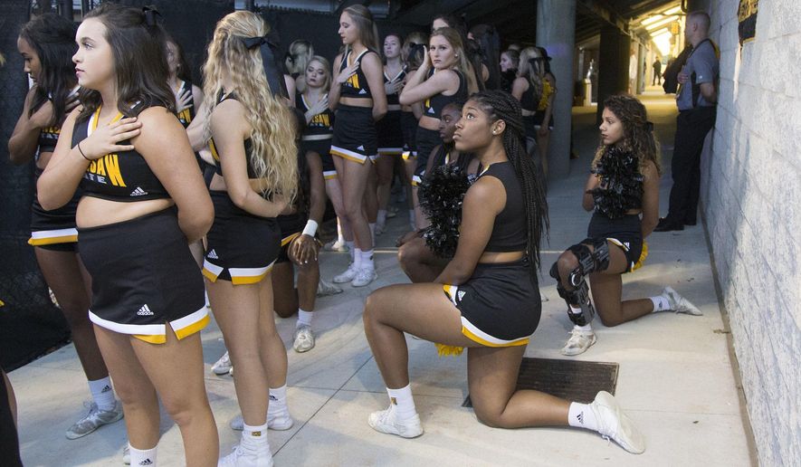 In this Saturday, Oct. 21, 2017, file photo, Four of the five Kennesaw State cheerleaders who took a knee three weeks ago during the Kennesaw State football game, take a knee once again out of sight of the fans under the visitors&#39; bleachers, during the national anthem before an NCAA college football game between Kennesaw State and Gardner-Webb in Kennesaw, Ga. Kennesaw State, which moved its football cheerleaders inside a stadium tunnel after a group of black cheer squad members knelt during the national anthem, has decided to let them again take the field during pre-game ceremonies. (Kelly J. Huff/The Marietta Daily Journal via AP, File)