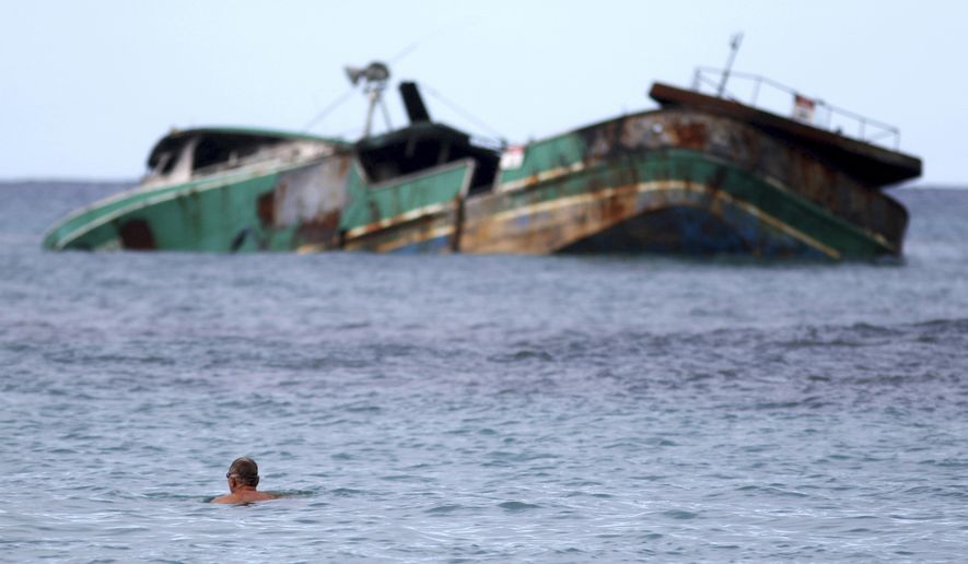 In this Wednesday, Nov. 8, 2017 photo, a swimmer looks at the Pacific Paradise, a commercial fishing vessel that ran aground about a month ago off Kaimana Beach in Honolulu. The fishing boat, which was transporting foreign workers to Hawaii when it smashed into a shallow reef just off the shores of Waikiki, has been leaking oil and fuel into the ocean as beachgoers swim nearby. (AP Photo/Caleb Jones)