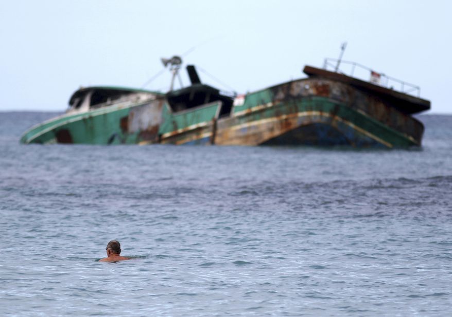 In this Wednesday, Nov. 8, 2017 photo, a swimmer looks at the Pacific Paradise, a commercial fishing vessel that ran aground about a month ago off Kaimana Beach in Honolulu. The fishing boat, which was transporting foreign workers to Hawaii when it smashed into a shallow reef just off the shores of Waikiki, has been leaking oil and fuel into the ocean as beachgoers swim nearby. (AP Photo/Caleb Jones)
