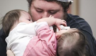 Nick Torres hugs his daughters, conjoined twins, Carter, left, and Callie at the Utah Center For Assistive Technology in Salt Lake City, on Nov. 6, 2017. The Utah Center for Assistive Technology is having a fitting for a specialized jumper made for conjoined twins.  The device is the first to help the girls into a standing position with no assistance.   (Adam Fondren/The Deseret News via AP)