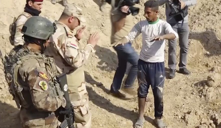In this Saturday, Nov. 11, 2017 frame grab from video, Iraqi security forces speak to shepherd Khalaf Luhaibi next to bones on the ground, in an area recently retaken from the Islamic State group, at an abandoned base near the northern town of Hawija, Iraq. Kirkuk governor Rakan Saed said Sunday that the bodies of civilians and security forces have been found at the mass grave that could contain up to 400 bodies. (Kirkuk Governor&#39;s Office via AP)