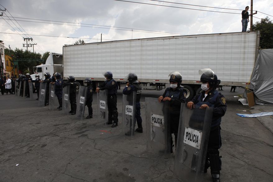 FILE - In this Sept. 1, 2010 file photo, police wearing face-masks guard a truck that arrived carrying the bodies of some of the 72 migrants who were killed in northern Mexico while trying to reach the US border, at a funeral home in Mexico City. Prosecutors said police and military personnel arrested on Tuesday, Nov. 14, 2017 an “old school” Zetas leader Martiniano Jaramillo who allegedly coordinated the 2010 killing spree that included the massacre of 72 Central American migrants in San Fernando in the border state of Tamaulipas. (AP Photo/Eduardo Verdugo, File)