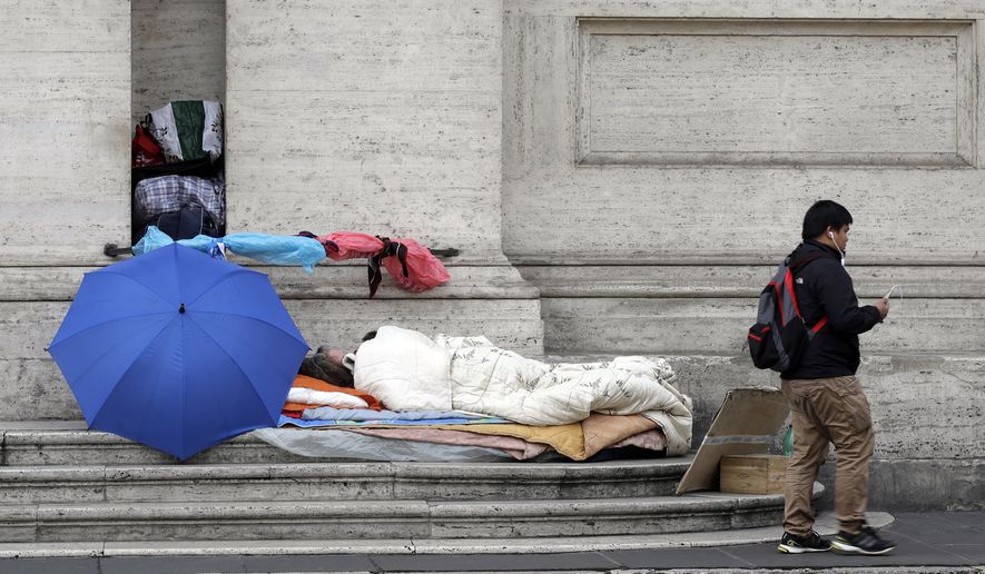 In this photo taken Thursday, Nov. 16, 2017, a man walks past a homeless sleeping on the steps of a building, in Rome. On the morning of Sunday, Nov. 19, 2017, Pope Francis will host some four thousand poor and vulnerable people in St Peter&#x27;s Basilica and after a Mass 1.500 of the guests will have lunch with the him in the Paul VI hall in what the pontiff called World Day of the Poor. (AP Photo/Alessandra Tarantino)