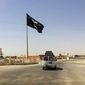 A motorist passes by a flag of the Islamic State group in central Rawah, 175 miles (281 kilometers) northwest of Baghdad, on July 22, 2014. (Associated Press) **FILE**