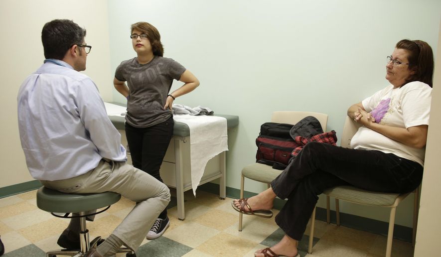 In this Thursday, Oct. 8, 2015, photo, Theo Ramos, 14, center, talks with endocrinologist Dr. Alejandro Diaz, center, accompanied by his mother, Lori, in Miami. Doctors say going slow when treating trans teens is essential for their physical and emotional well-being, and note that if a teen’s feelings last until age 16, their desires are probably permanent. (AP Photo/Lynne Sladky) **FILE**