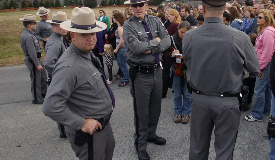 FILE--This photo from Tuesday, Nov. 10, 2009 shows New York State Police waiting with families for students to be released after a lockdown at Stissing Mountain Middle School and High School in Pine Plains, N.Y. The president of the National Association of School Resource Officers says schools regularly practice safety plans and have gotten good at taking action anytime they hear about a potential threat in or outside the building. (AP Photo/Mike Groll, File)