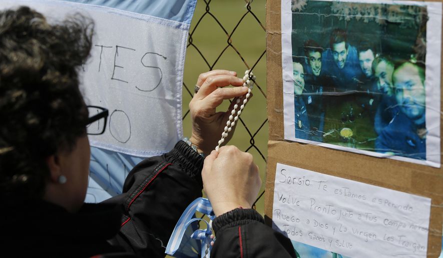 A woman wraps a rosary on the link of a fence blanketed with national flags in support of the crew members of the lost submarine, on the perimeters of the naval base in Mar del Plata, Argentina, Tuesday, Nov. 21, 2017. The ARA San Juan Argentine submarine has been lost at sea last week with 44 crew members on board as it was on a voyage from the extreme southern port of Ushuaia to the city of Mar del Plata.(AP Photo/Vicente Robles)