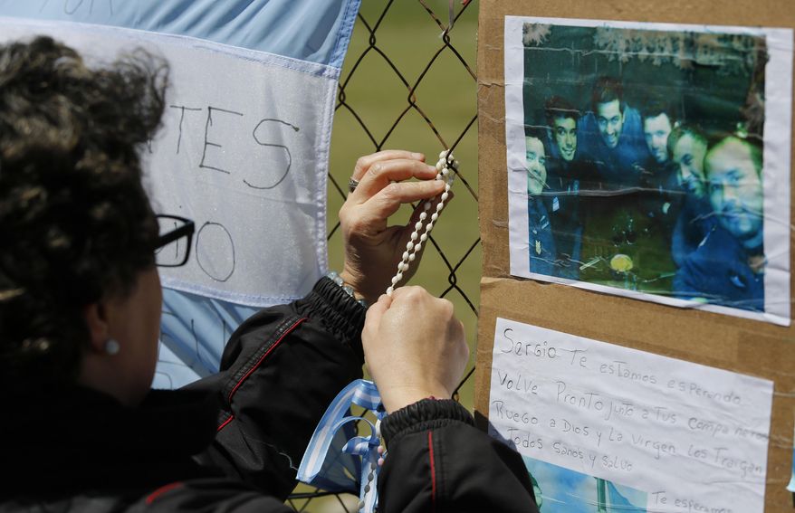 A woman wraps a rosary on the link of a fence blanketed with national flags in support of the crew members of the lost submarine, on the perimeters of the naval base in Mar del Plata, Argentina, Tuesday, Nov. 21, 2017. The ARA San Juan Argentine submarine has been lost at sea last week with 44 crew members on board as it was on a voyage from the extreme southern port of Ushuaia to the city of Mar del Plata.(AP Photo/Vicente Robles)