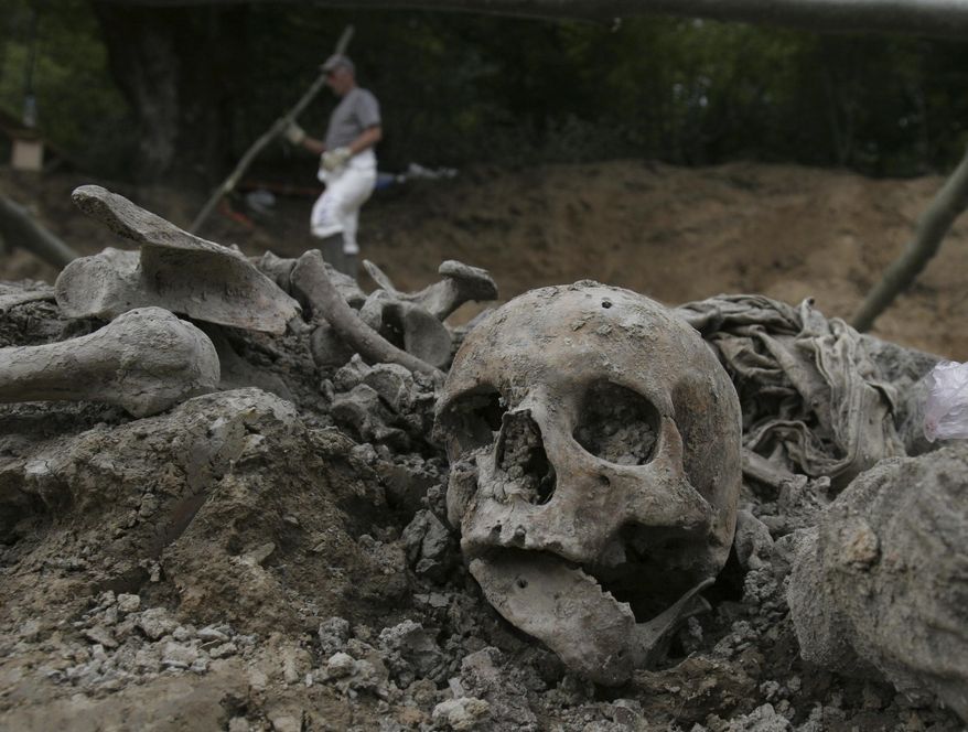 A July 10, 2007, file photo shows a Bosnian worker passing by a human skull during exhumation at a mass grave site in a village of Budak, near Srebrenica, Bosnia-Herzegovina. (AP Photo/Amel Emric, File)