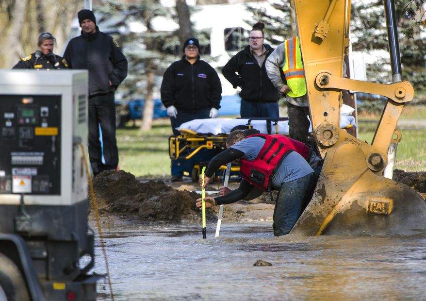Emergency crews attempt to save a construction worker who became trapped in a flooded hole after a water main broke in Burton, Mich., on Tuesday, Nov. 21, 2017. The man, who was trapped underwater for roughly 20 minutes, did not have a pulse when he was taken to the hospital but medical personnel were able to re-establish a heartbeat, according to Burton police Chief Tom Osterholzer. He is listed in extremely critical condition. (Terray Sylvester/MLive.com via AP)