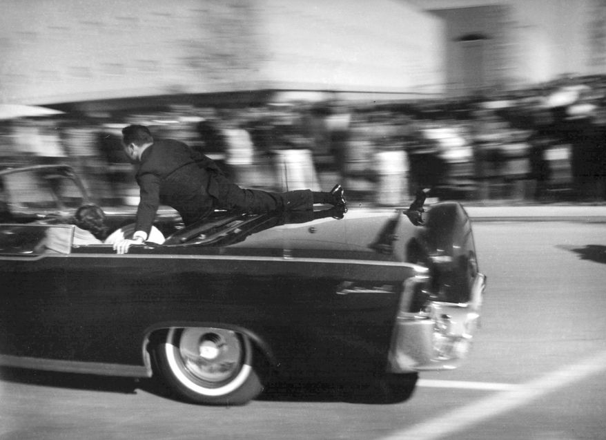 In this Nov. 22, 1963 file photo, the limousine carrying mortally wounded President John F. Kennedy races toward the hospital seconds after he was shot in Dallas. Secret Service agent Clinton Hill is riding on the back of the car, Nellie Connally, wife of Texas Gov. John Connally, bends over her wounded husband, and first lady Jacqueline Kennedy leans over the president. (AP Photo/Justin Newman, File)