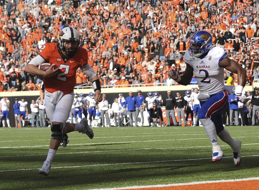 Kansas defensive end Dorance Armstrong Jr., right, chases after Oklahoma State quarterback Mason Rudolph as he scores a touchdown in the first half of an NCAA college football game between Kansas and Oklahoma St in Stillwater, Okla., Saturday, Nov. 25, 2017. (AP Photo/Brody Schmidt)