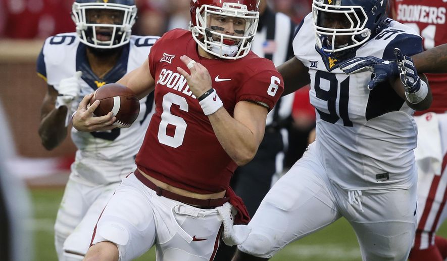 Oklahoma quarterback Baker Mayfield (6) carries past West Virginia safety Dravon Askew-Henry (6) and defensive lineman Ezekiel Rose (91) in the second quarter of an NCAA college football game in Norman, Okla., Saturday, Nov. 25, 2017. (AP Photo/Sue Ogrocki)