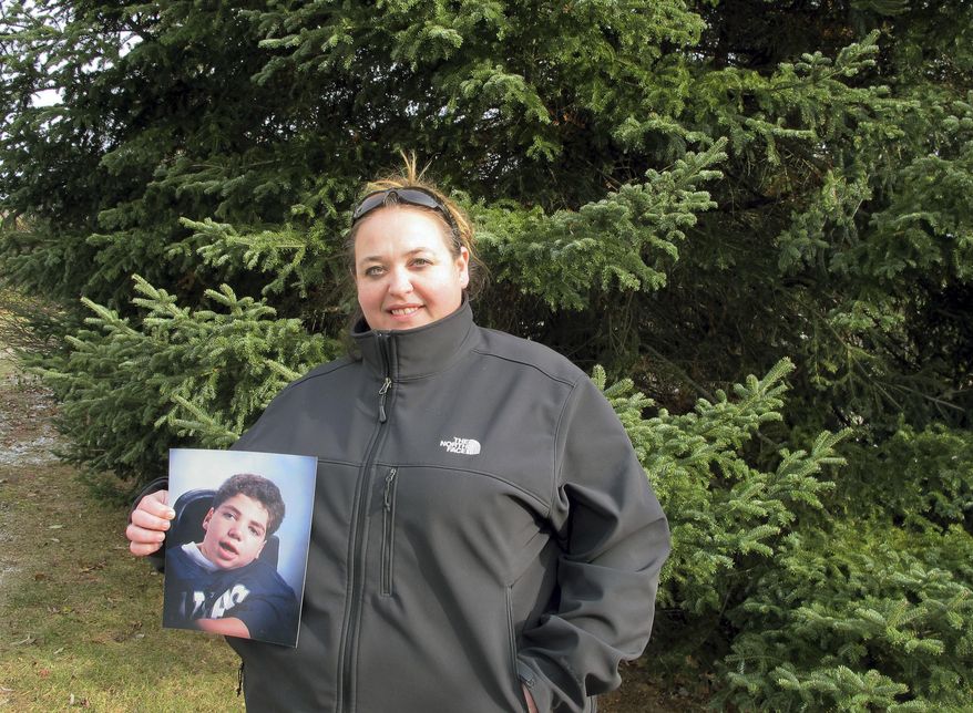 Marie Eugair poses with a photograph of her late adopted brother John Paul Greene-Eugair in Pittsford, Vt., on Tuesday, Nov. 28, 2017, in front a tree he helped plant 26 years ago. The tree was cut down on Tuesday to become Vermont's state Christmas tree. The Eugairs donated the tree in a tribute to the boy who died of complications from cerebral palsy in 1995 at age 16. (AP Photo/Lisa Rathke)
