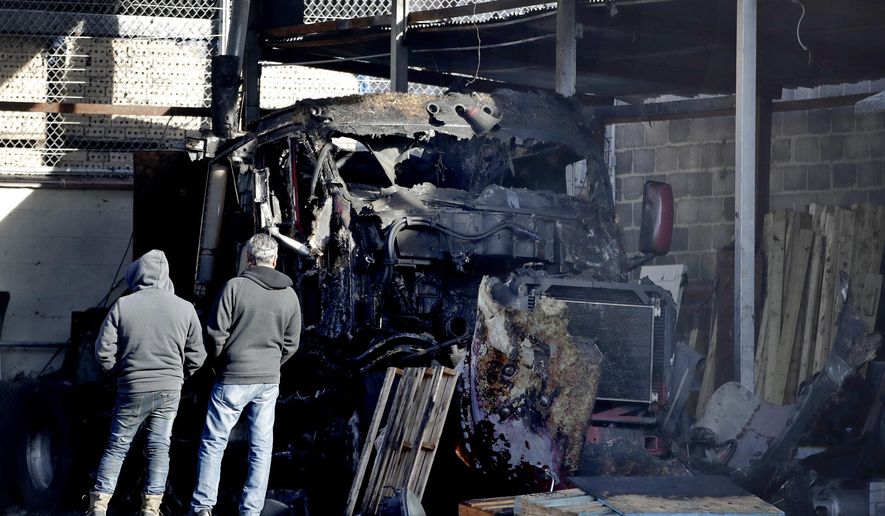 Two men look at a charred semi-tractor trailer following an early morning fire at a business, Tuesday, Nov. 28, 2017, in Newark, N.J. A vehicle and part of the commercial building also caught on fire. No injuries were reported. (AP Photo/Julio Cortez)