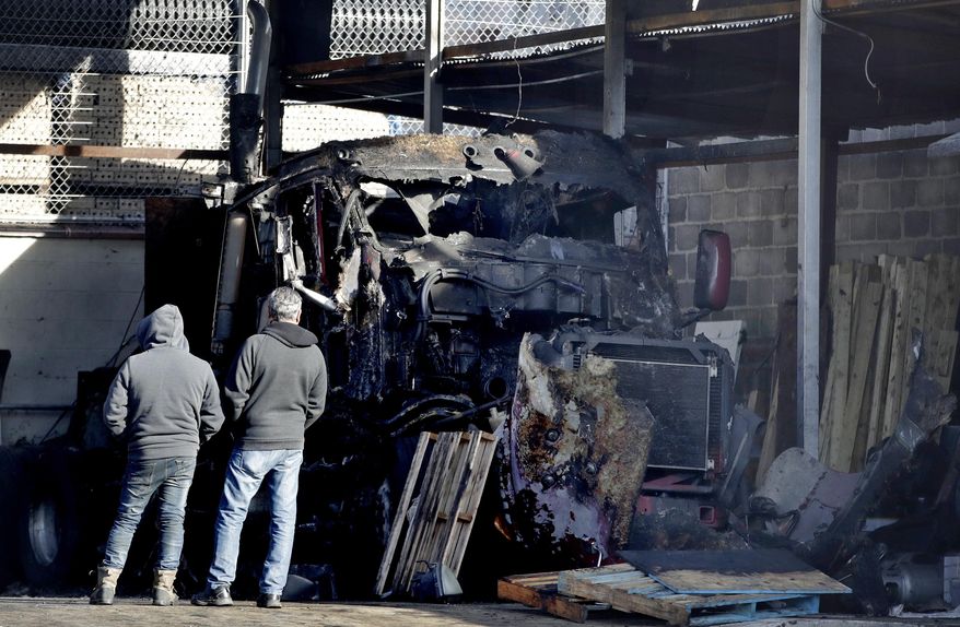 Two men look at a charred semi-tractor trailer following an early morning fire at a business, Tuesday, Nov. 28, 2017, in Newark, N.J. A vehicle and part of the commercial building also caught on fire. No injuries were reported. (AP Photo/Julio Cortez)