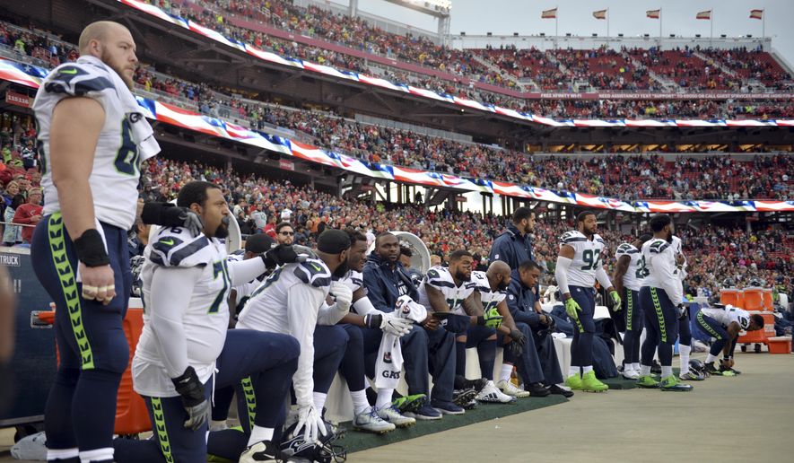 FILE - In this Nov. 26, 2017, file photo, Seattle Seahawks players sit and kneel during the playing of the national anthem before an NFL football game against the San Francisco 49ers, in Santa Clara, Calif. President Donald Trump is renewing his complaints about NFL players who kneel during the national anthem. Players have been kneeling to protest racism and police brutality, particularly toward people of color. Trump says the act is disrespectful and is hurting the game.(AP Photo/Don Feria, File)