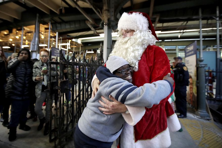 Domore Walker, 14, left, a student at West Caldwell Tech, gives a hug to a man wearing a Santa Claus suit before riding on a New Jersey Transit train at the Hoboken Terminal, Friday, Dec. 1, 2017, in Hoboken, N.J. Schoolchildren were picked up by the train at various stations as part of the agency's annual Railmen For Children Santa Train. (AP Photo/Julio Cortez)