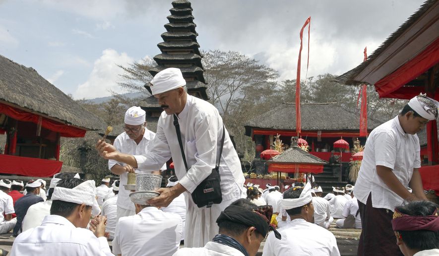 Hindu priests give holy water to worshipers during a prayer at a temple located a few kilometers (miles) from the crater of the Mount Agung volcano in Karangasem, Bali, Indonesia, Sunday, Dec. 3, 2017. Authorities have told tens of thousands of people to leave an area extending 10 kilometers (6 miles) from the volcano as it belches volcanic materials into the air. Mount Agung's last major eruption in 1963 killed about 1,100 people. (AP Photo/Firdia Lisnawati)