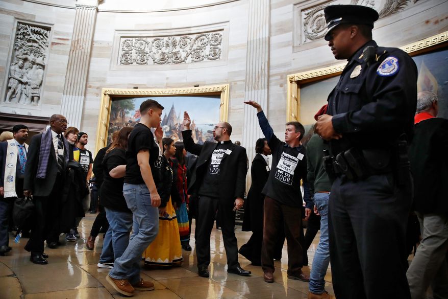 With shirts saying &quot;fight poverty not the poor,&quot; people with the &quot;Poor People&#39;s Campaign&quot; gesture the group to remain quiet as the group leaves the Capitol Rotunda after praying in an act of civil disobedience in protest of the Republican tax overhaul on Monday. (Associated Press)