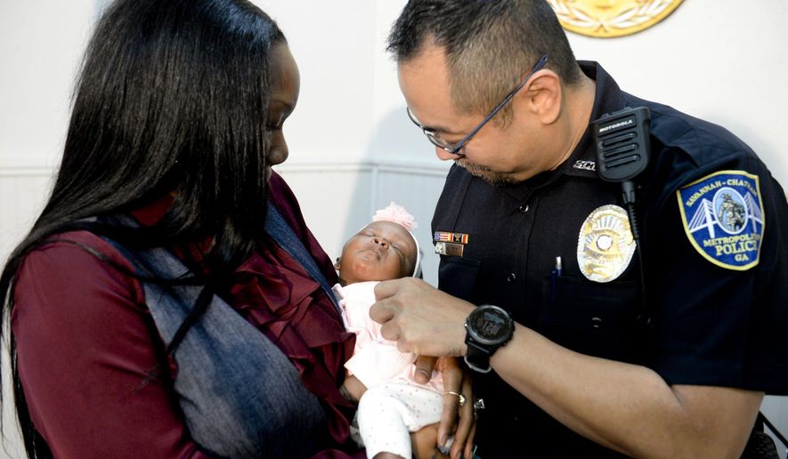 Savannah-Chatham police officer William Eng, right, plays with 29-day-old Bella Adkins while her mother, Tina Adkins, holds her on Monday, Dec. 4, 2017, at Savannah-Chatham police headquarters. Eng performed life-saving CPR on the infant on Friday. (Will Peebles/Savannah Morning News via AP)