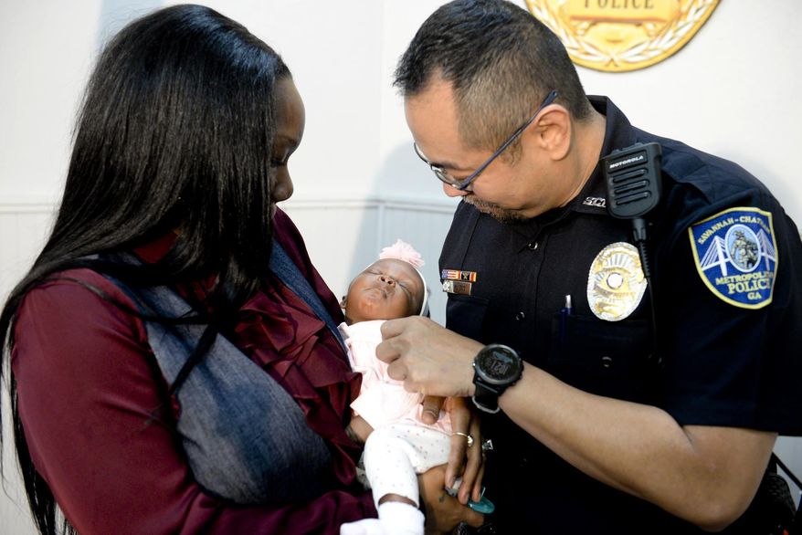 Savannah-Chatham police officer William Eng, right, plays with 29-day-old Bella Adkins while her mother, Tina Adkins, holds her on Monday, Dec. 4, 2017, at Savannah-Chatham police headquarters. Eng performed life-saving CPR on the infant on Friday. (Will Peebles/Savannah Morning News via AP)