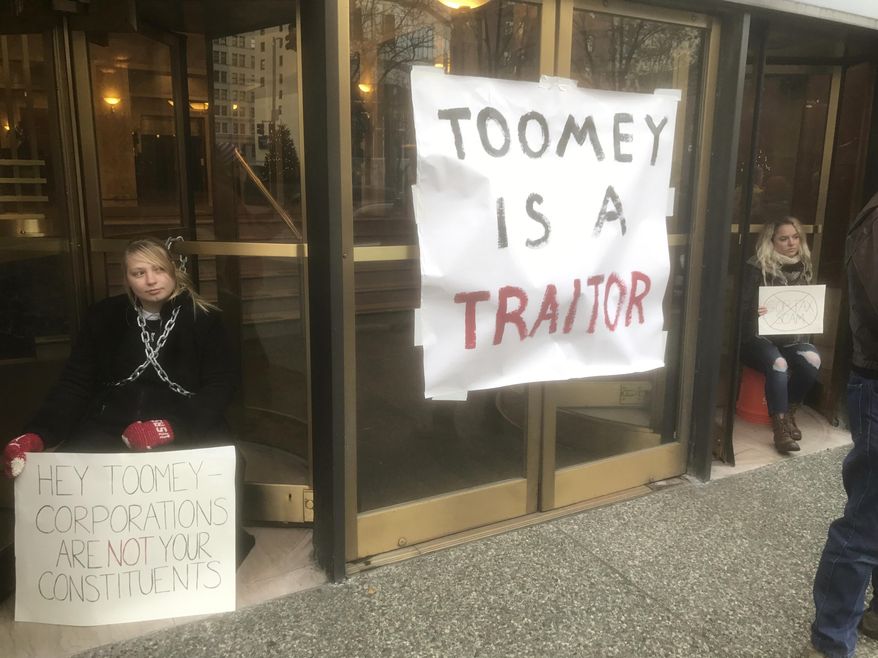 Protesters Lindsey Disler, left, and Chelsey Engel chain themselves to the entrance of 310 Grant Street where U.S. Sen. Pat Toomey has his local office to protest the Senate's tax bill in Pittsburgh, Monday, Dec. 4, 2017. (Darrell Sapp/Pittsburgh Post-Gazette via AP)