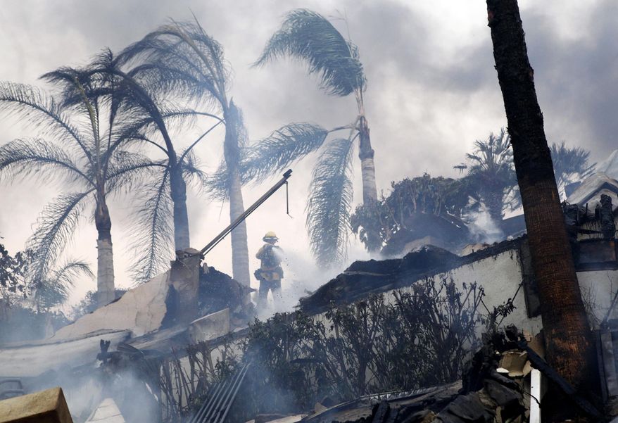 A firefighter stands under windswept palm trees as he hoses down smoldering debris in Ventura, Calif., Tuesday, Dec. 5, 2017. Ferocious Santa Ana winds raking Southern California whipped explosive wildfires Tuesday, prompting evacuation orders for thousands of homes. (Daniel Dreifuss via AP)