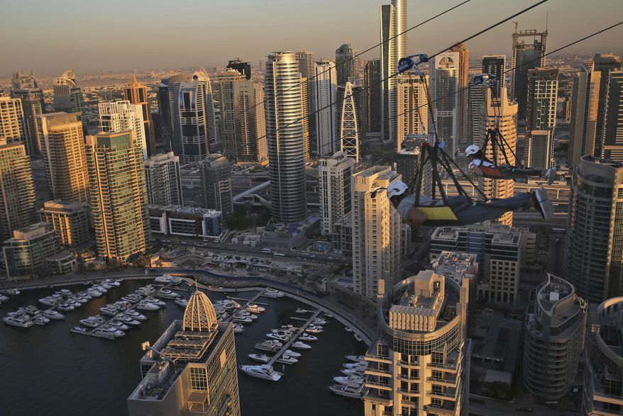 Two people ride the world's longest urban zip line with a speed of up to 80 kilometers per hour on a one kilometer run from 170 meter to ground level, at the Marina district of Dubai, United Arab Emirates, Tuesday, Dec. 5, 2017. (AP Photo/Kamran Jebreili)