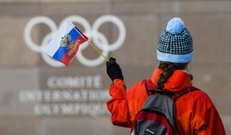 A woman waves a Russian flag outside of the International Olympic Committee (IOC) headquarters in front of the Olympic Rings prior to the opening of the first day of the executive board meeting of the International Olympic Committee (IOC) at the IOC headquarters, in Pully near Lausanne, on Tuesday, Dec. 5, 2017.  Russian athletes will be allowed to compete at the upcoming Pyeongchang Olympics as neutrals despite orchestrated doping at the 2014 Sochi Games, the International Olympic Committee said Tuesday. (Jean-Christophe Bott, Keystone via AP)