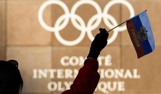 A woman waves a Russian flag outside of the International Olympic Committee (IOC) headquarters in front of the Olympic Rings prior to the opening of the first day of the executive board meeting of the International Olympic Committee (IOC) at the IOC headquarters, in Pully near Lausanne, on Tuesday, Dec. 5, 2017.  Russian athletes will be allowed to compete at the upcoming Pyeongchang Olympics as neutrals despite orchestrated doping at the 2014 Sochi Games, the International Olympic Committee said Tuesday. (Jean-Christophe Bott, Keystone via AP)