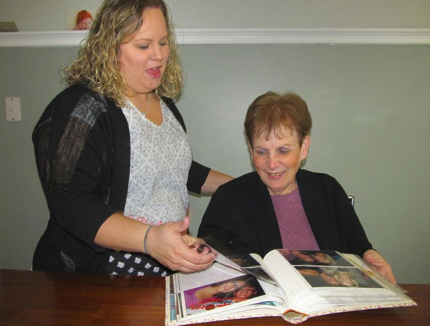 In this Nov. 21, 2017 photo Jessica Carmany, left, and her mother, Bonnie Bury, glance at a family photo album, which includes pictures of Bury's mother, Lucille Falley at Carmany's home in Bloomington, Ill. Bury is her mother's caregiver who has dementia. Bury doesn't consider herself a caregiver to Falley, even though she handles her mother's finances, oversees her medical care and living arrangements, takes her to doctors' appointments, attends all her care plan meetings, and spends time with her three times a week. "I consider myself a behind-the-scenes caregiver," Bury said.(Paul Swiech/The Pantagraph via AP)