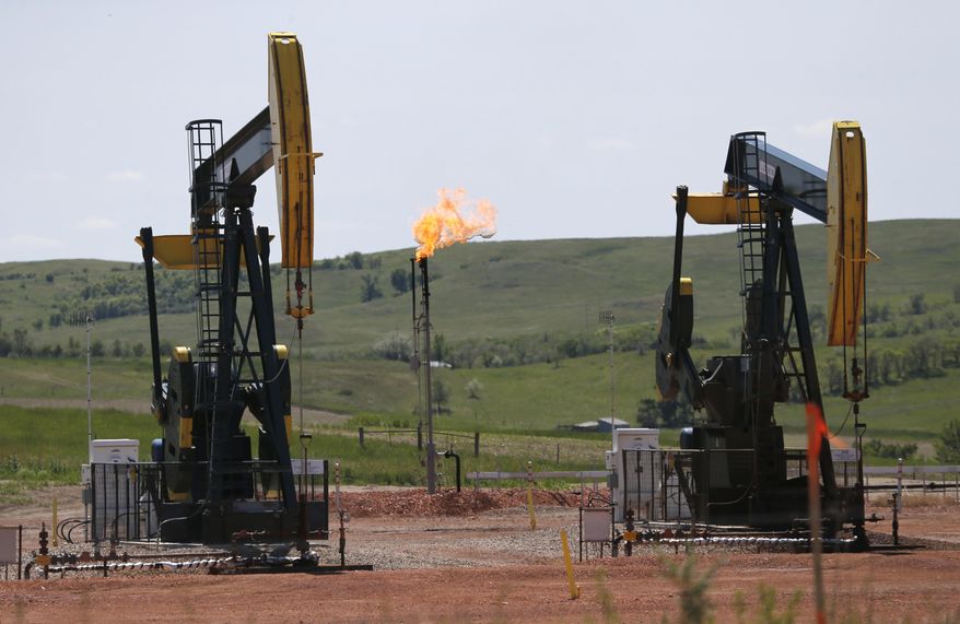 FILE - In this June 12, 2014, file photo, oil pumps and natural gas burn off in Watford City, N.D. The Interior Department is delaying an Obama-era regulation aimed at restricting harmful methane emissions from oil and gas production on federal lands. A rule being published Dec. 8, delays the methane regulation until January 2019, calling the previous rule overly burdensome to industry.  (AP Photo/Charles Rex Arbogast, File)