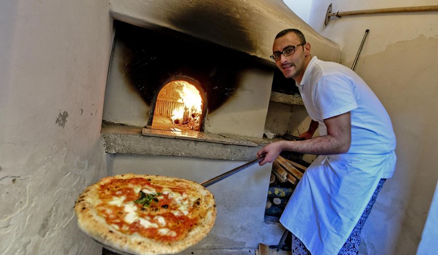 A man shows a pizza cooked in the first stone oven which was used in the 1889 to make the first pizza Margherita in Naples, Italy, Wednesday, Dec. 6, 2017. Italy is waiting a decision by the United Nations Educational, Scientific and Cultural Organisation (UNESCO) to recognize to the Neapolitan pizza in the intangible cultural heritage list. (Ciro Fusco/ANSA Via AP)