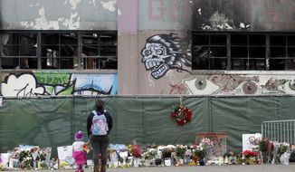 FILE - This Dec. 13, 2016 file photo shows flowers, pictures, signs and candles, are placed at the scene of a warehouse fire in Oakland, Calif. A former tenant of an Oakland warehouse says police were called to the unlicensed residence several times to help with evictions, and even knew the leaseholder by name. Jose Avalos, a woodworker who moved into the Ghost Ship two years before a deadly fire killed 36 partygoers a year ago, testified Thursday, Dec. 7, 2017, on the second day of a preliminary hearing in Alameda County Superior Court for two men charged with involuntary manslaughter in their deaths. (AP Photo/Marcio Jose Sanchez, File)