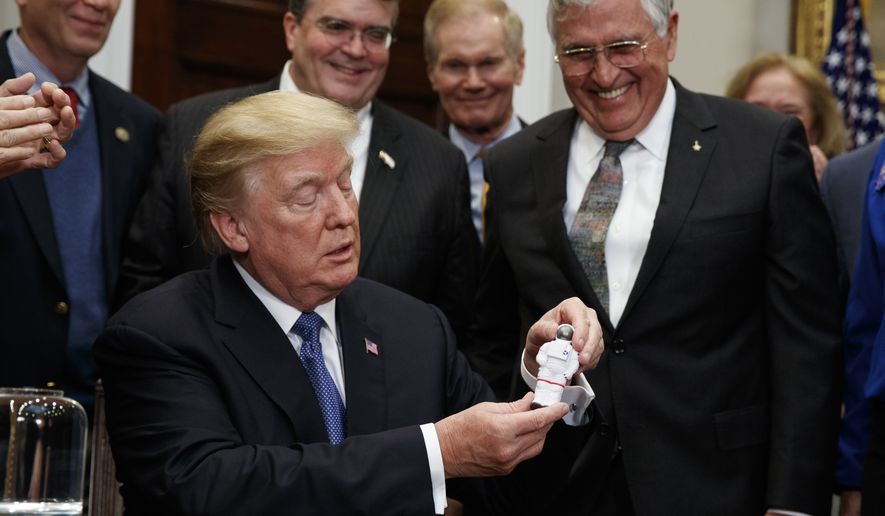 President Donald Trump holds up a figurine handed to him by former Apollo 17 astronaut Jack Schmitt, right, after signing a policy directive to send American astronauts back to the moon, and eventually Mars, in the Roosevelt Room of the White House, Monday, Dec. 11, 2017, in Washington. (AP Photo/Evan Vucci)