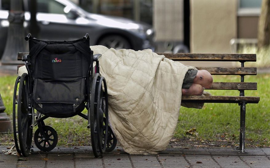FILE - In this Sept. 19, 2017, file photo, a person sleeps next to a wheelchair on a park bench in downtown Portland, Ore., not far from the city's trendy Pearl District. An annual report found that 80 homeless people died on the streets of Portland and the surrounding area in 2016. The number released Thursday, Dec. 14 is only a slight improvement over 2015, when 88 homeless people died outside. (AP Photo/Ted S. Warren, File)
