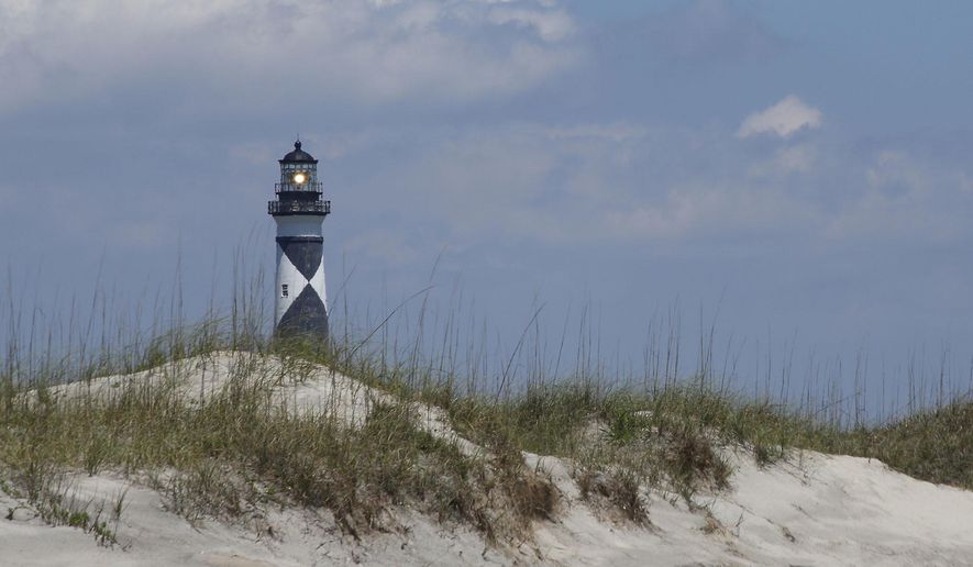 FILE - In this July 9, 2014 file photo, Cape Lookout Lighthouse shines its light over a sand dune from the Atlantic side in New Bern, N.C.  The national seashore in North Carolina invites the public to a climb of the Cape Lookout Lighthouse on New Year’s Day. A news release says space is limited and reservations are required.  (Bill Hand/Sun Journal via AP)