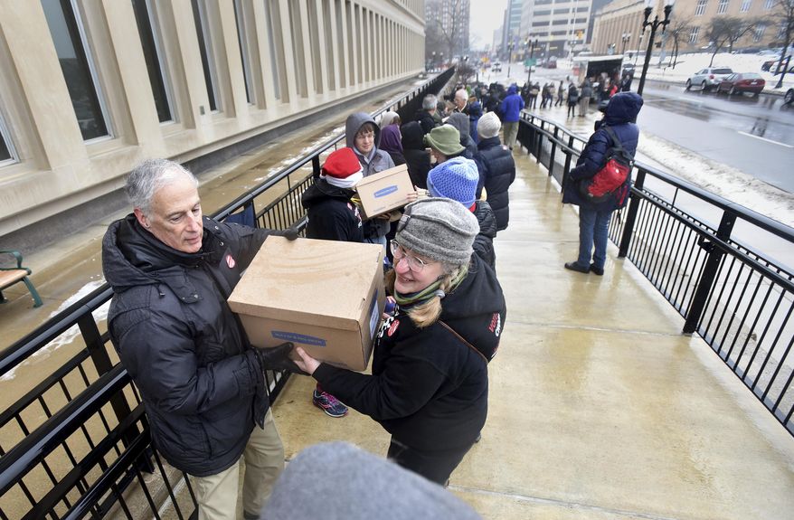 Jim Nelson of DeWitt, left, and Carolyn Hejkil of Scio Twp. Mich., team up to deliver petitions to change the way districts are created in Michigan arrive Monday, Dec 18, 2017, at the Secretary of State's office in Lansing. Mich., with over 400,000 signatures on them. Volunteers formed a human chain and handed the boxes from the truck, up the stairs and to the office. (Dale G Young/Detroit News via AP)