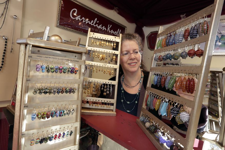 In this Thursday, Dec. 7, 2017, photo, Julie Siegmund, of Carnelian Knoll, looks at some of her earrings at her booth at the Union Square Holiday Market, in New York. At the holiday markets that pop up annually, many of the booths are staffed by artisans hoping to make a significant portion of their revenue or to get visibility that will translate into sales other times of the year. (AP Photo/Richard Drew)