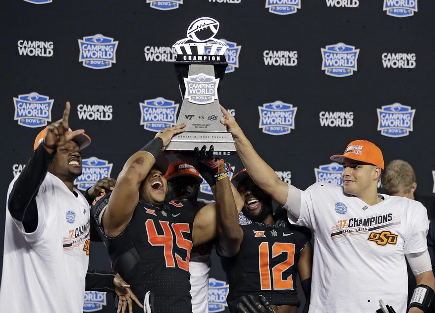 Oklahoma State players, from left, Tre Flowers, Chad Whitener (45), Kirk Tucker (12) and quarterback Mason Rudolph hold up the trophy after Oklahoma State defeated Virginia Tech 30-21 in the Camping World Bowl NCAA college football game Thursday, Dec. 28, 2017, in Orlando, Fla. (AP Photo/John Raoux)